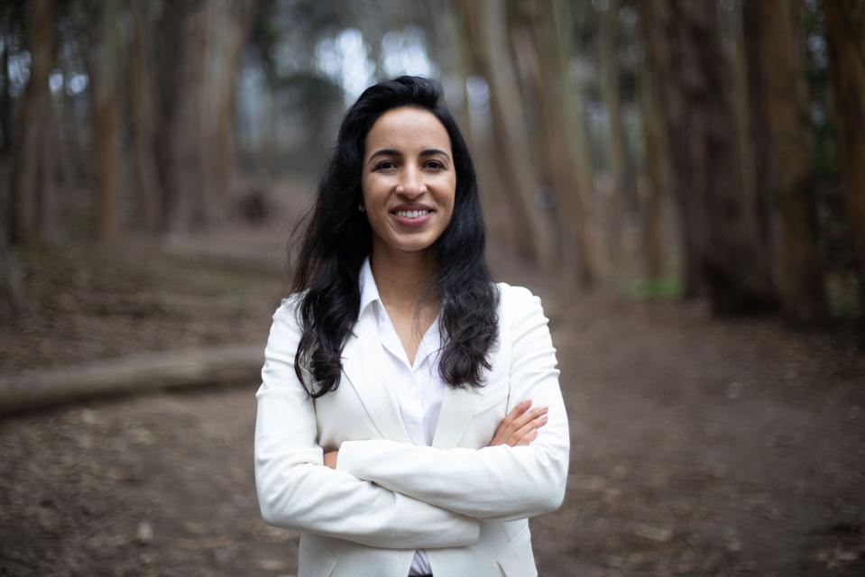 A woman in a white jacket with long dark hair smiling at camera