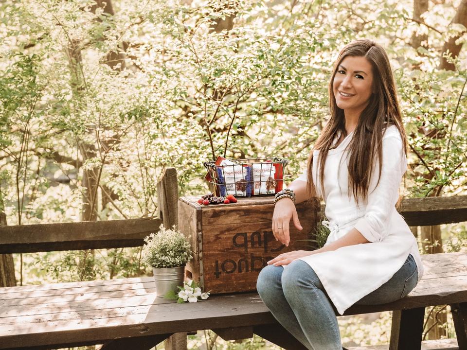 Poiesz sits at a picnic bench int he forest with a picnic basket under her arm.