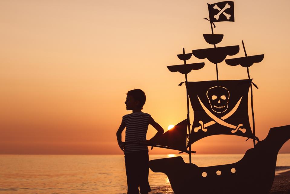 A little boy in silhouette at sunset with a pirate ship