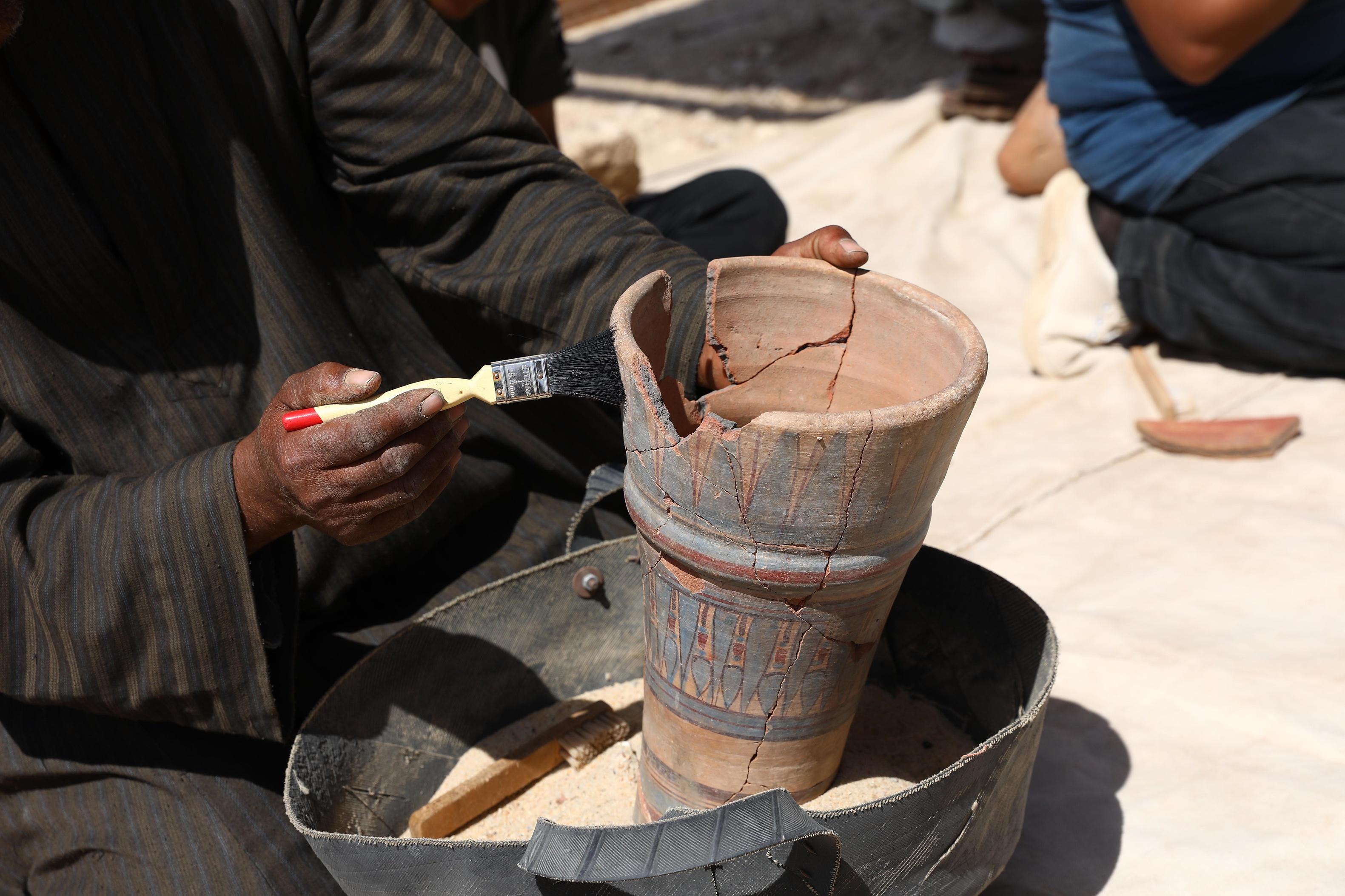 An excavation worker cleans a pottery vessel unearthed from the archeological site of the 