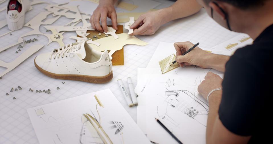 Two designers work on drawings for the Mylo Adidas white Stan Smith shoe.