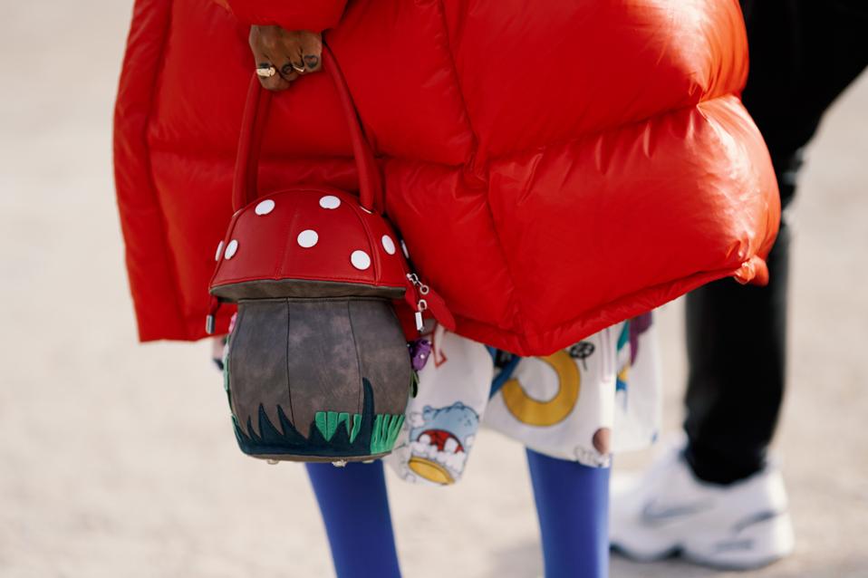 A model in a red parka holds a bag shaped like a mushroom.