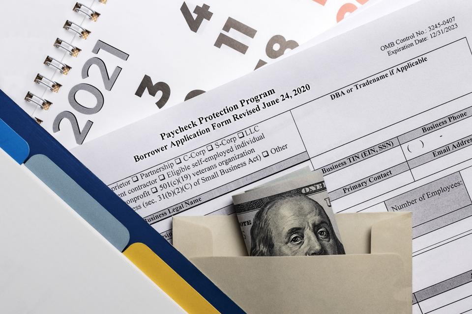 A PPP application form, envelope of money and planner sit on top of a 2021 calendar page.