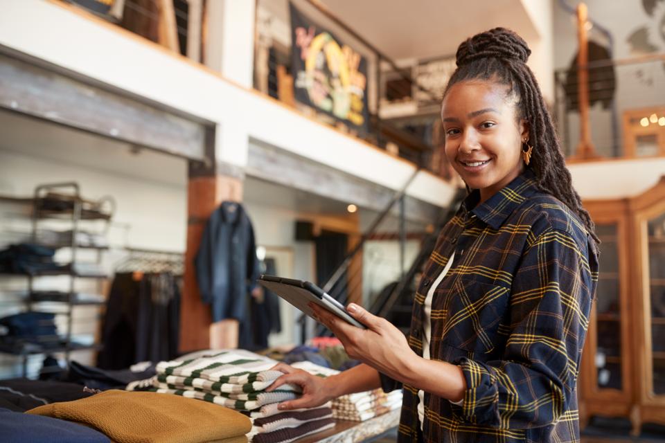 Portrait Of Female Owner Of Fashion Store Using Digital Tablet To Check Stock In Clothing Store