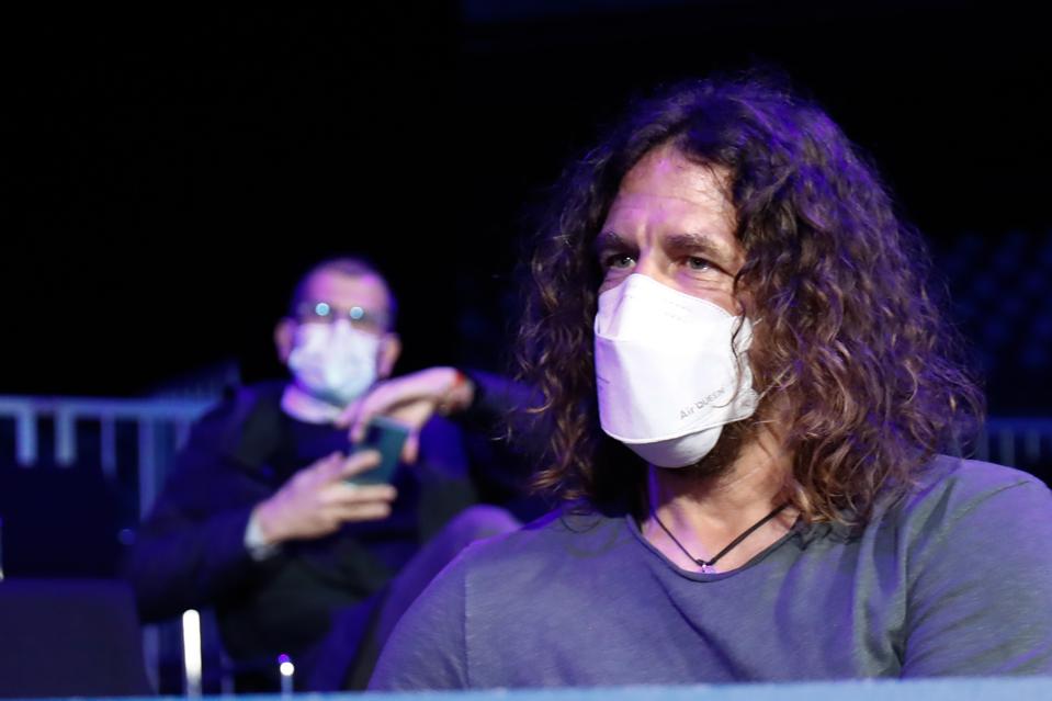 Carles Puyol sits indoors while wearing a white face mask.