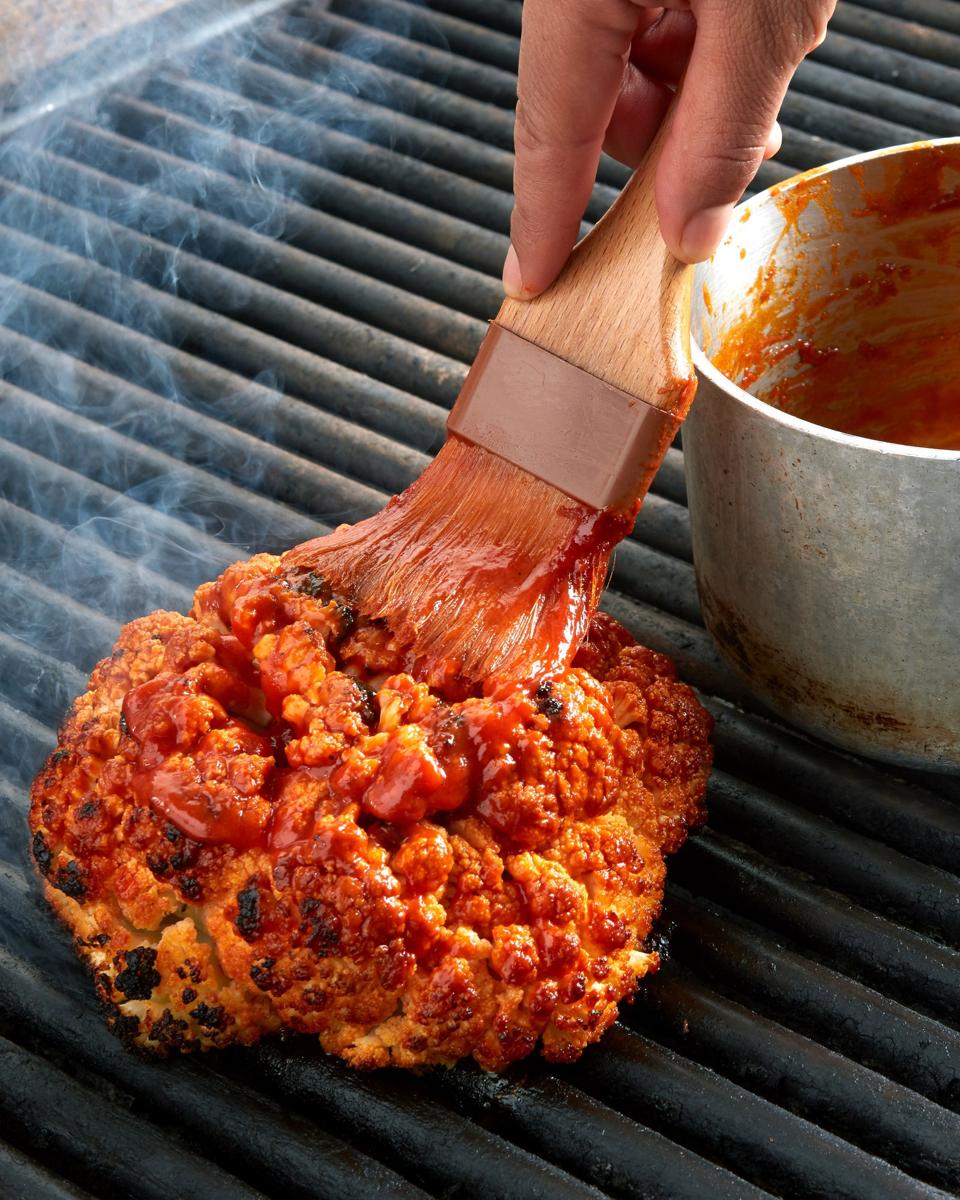 a whole cauliflower is doused in sauce and grilled with more sauce brushed on top