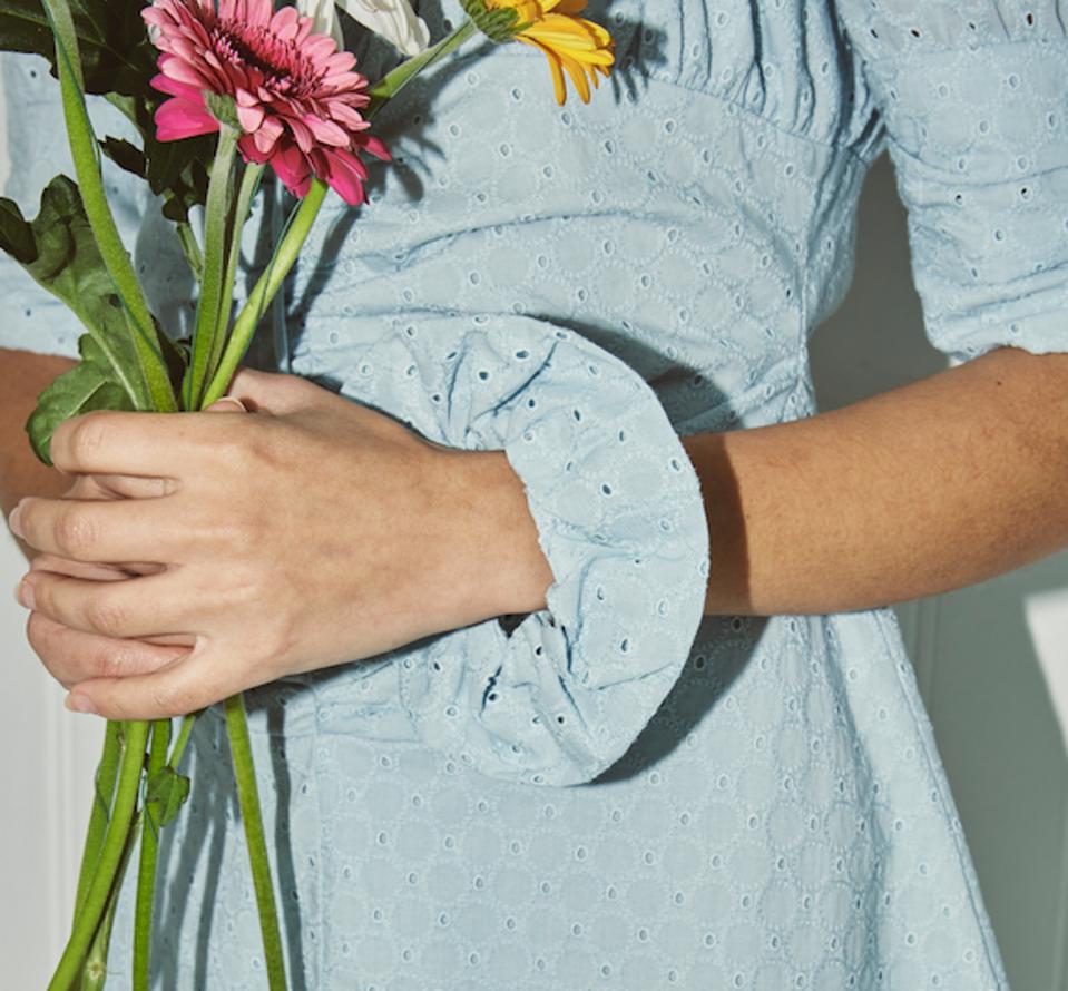 a woman wearing blue dress and scrunchie in same fabric holding a bunch of spring flowers