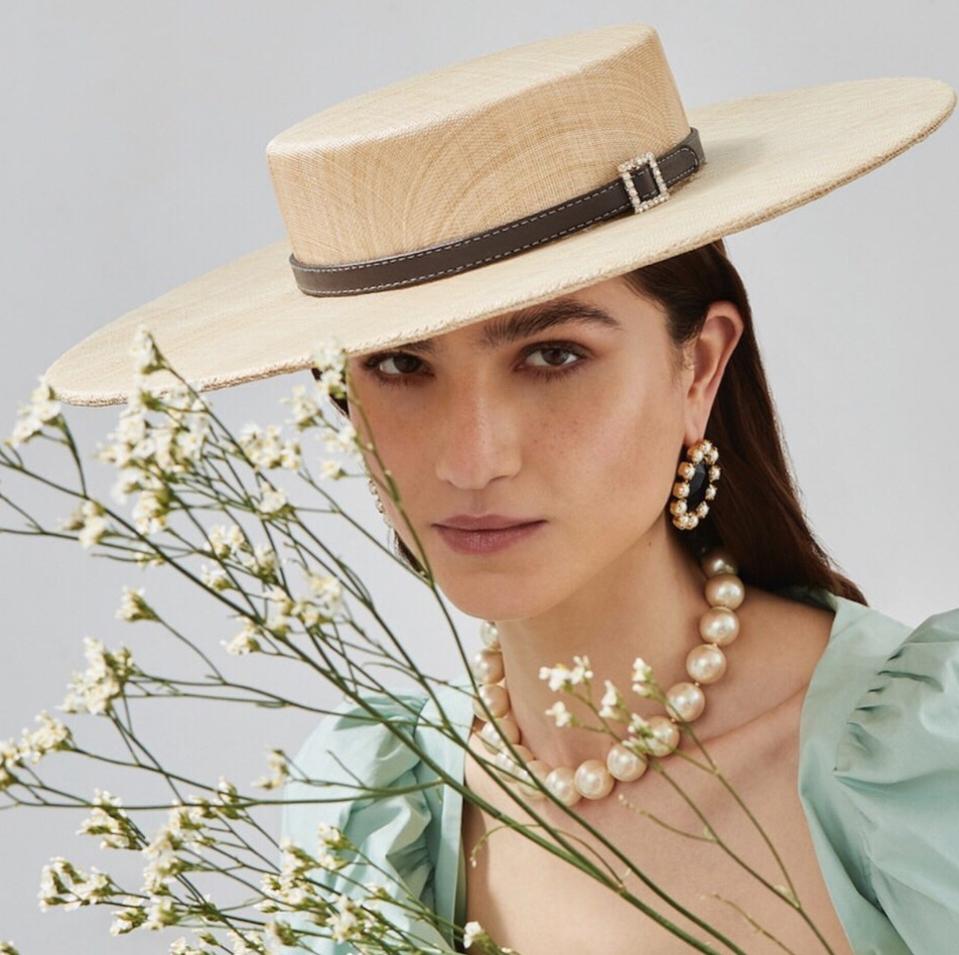 a brunette woman wearing a straw boater hat holding flowers