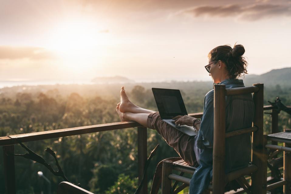 Business woman working on her laptop on a balcony outside facing sunset.