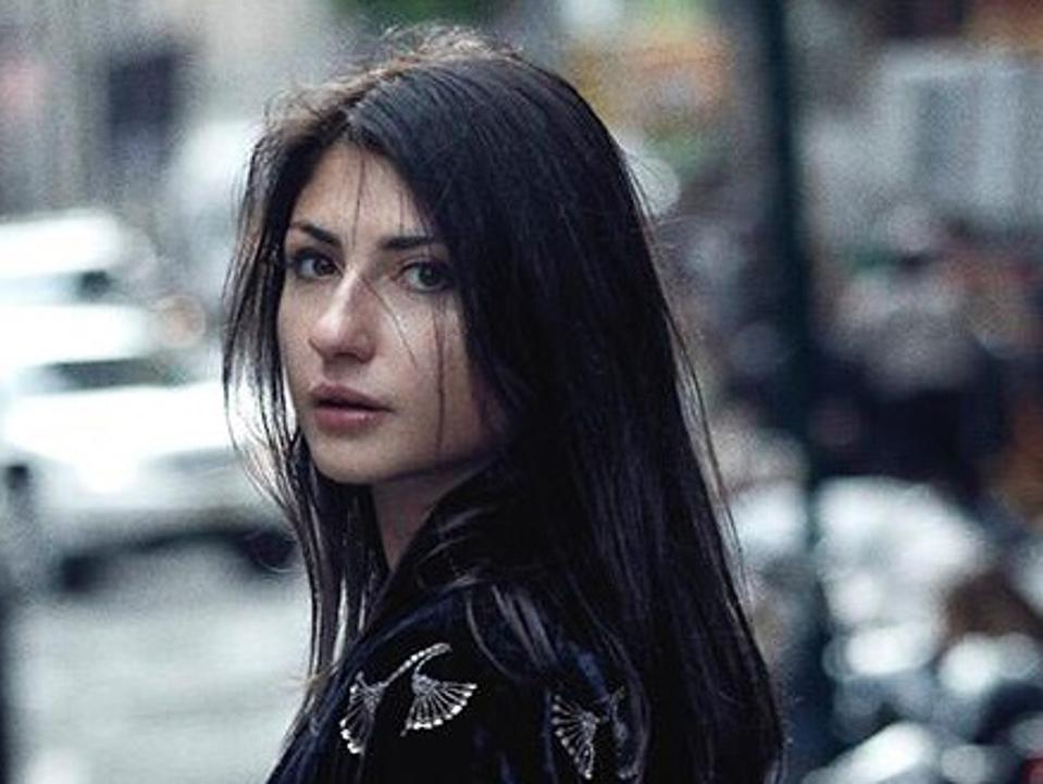 Headshot of Mella with long black hair walking on city street.