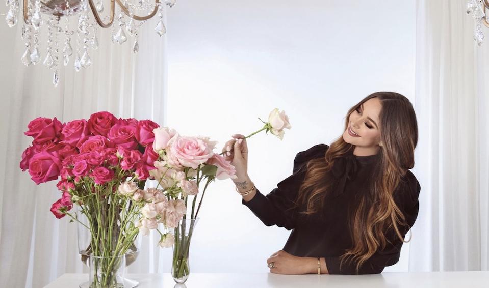 A brunette woman arranges roses on a white table.