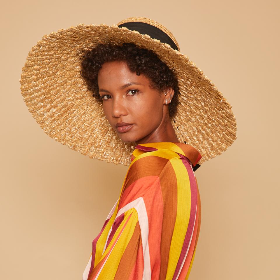 Une femme vêtue d'un chemisier aux couleurs vives porte le chapeau de paille naturelle Mirabel