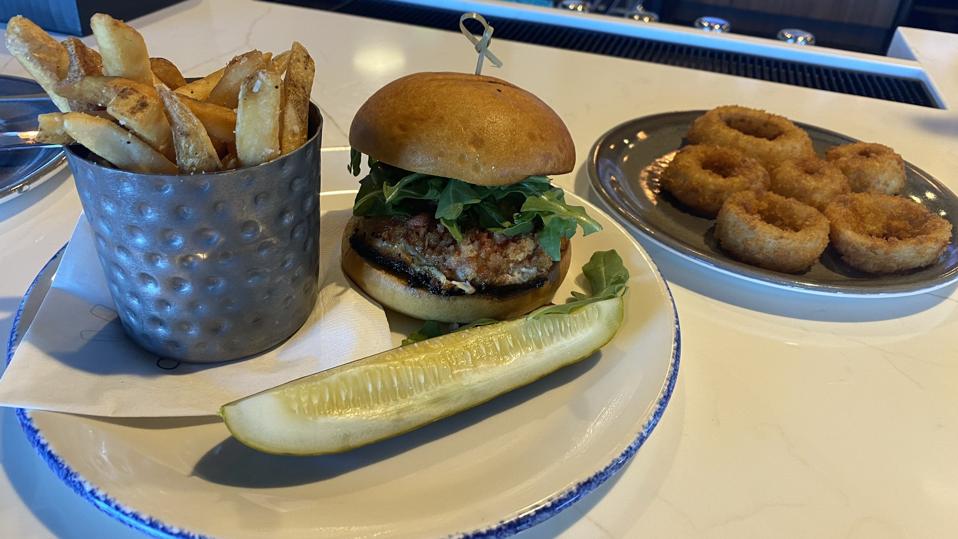 A plate with a burger, pickles, and fries on it, and a second plate with onion rings