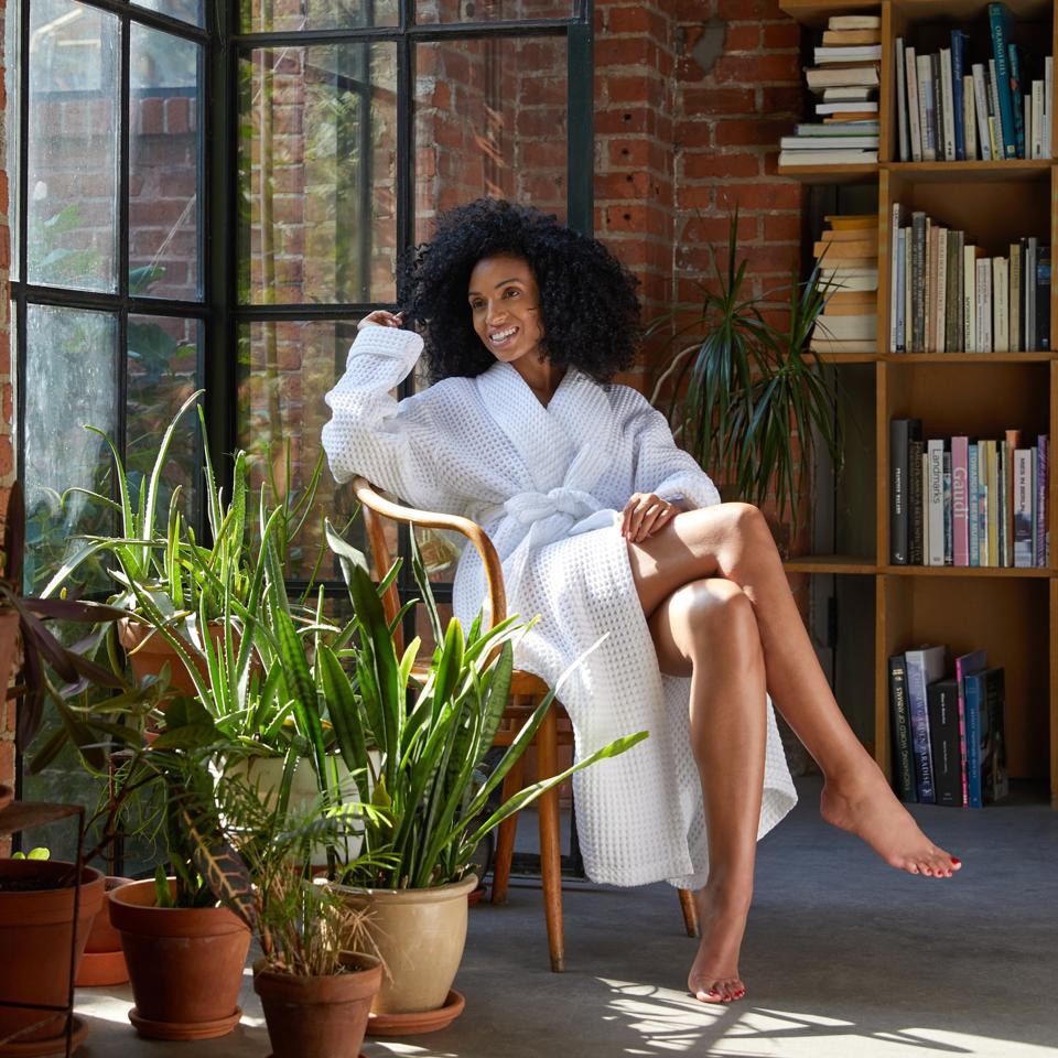 A woman sits in a chair wearing a white Brooklinen waffle robe.