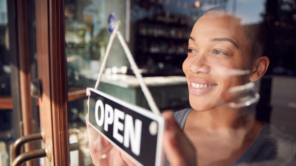 Female Owner Of Start Up Shop Or Restaurant Turning Round Open Sign On Door.