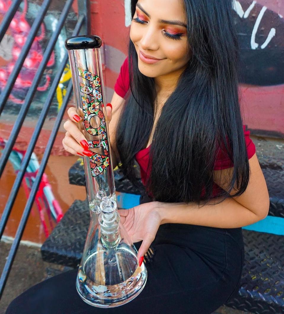 A woman sitting on a stoop displaying a Mexican Sugar Skull Bong from Mota Glass.