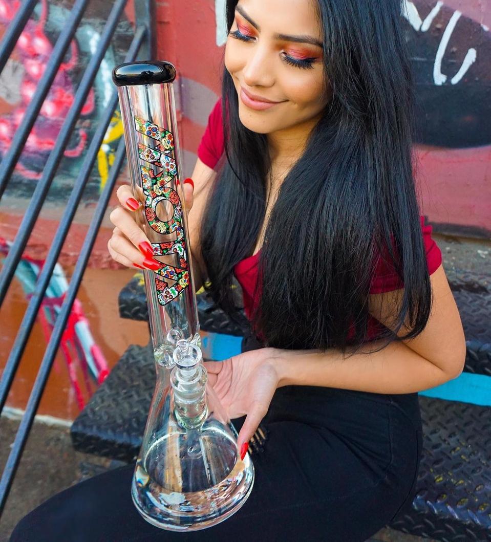 A woman sitting on a stoop displaying a Mexican Sugar Skull Bong from Mota Glass.