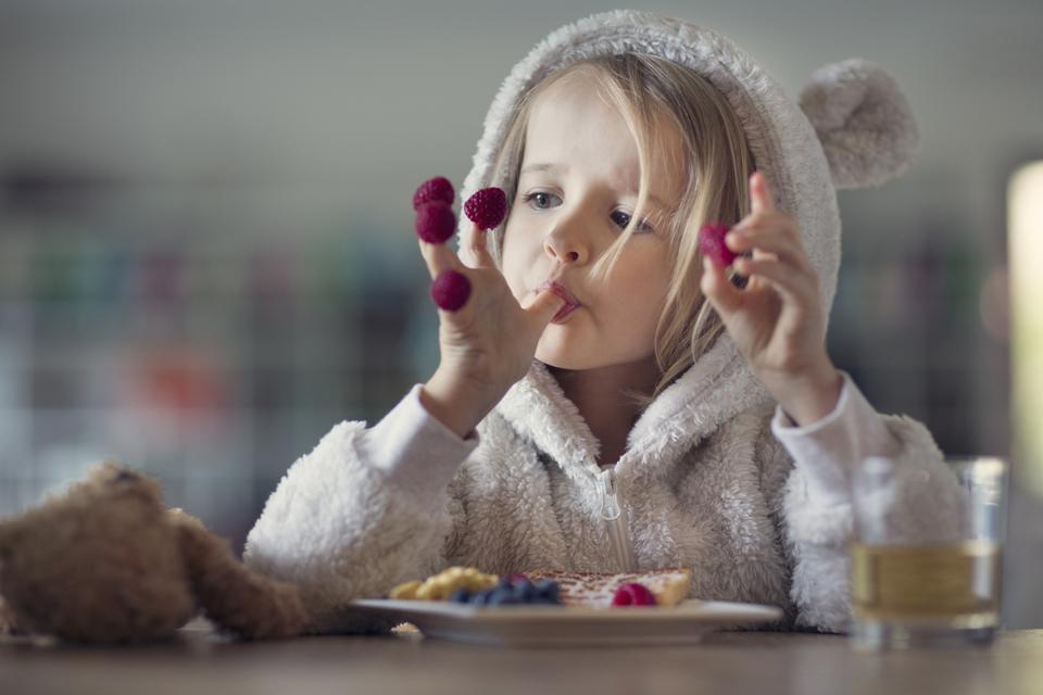 Girl in cozy hooded pyjamas, eating raspberries off her fingers