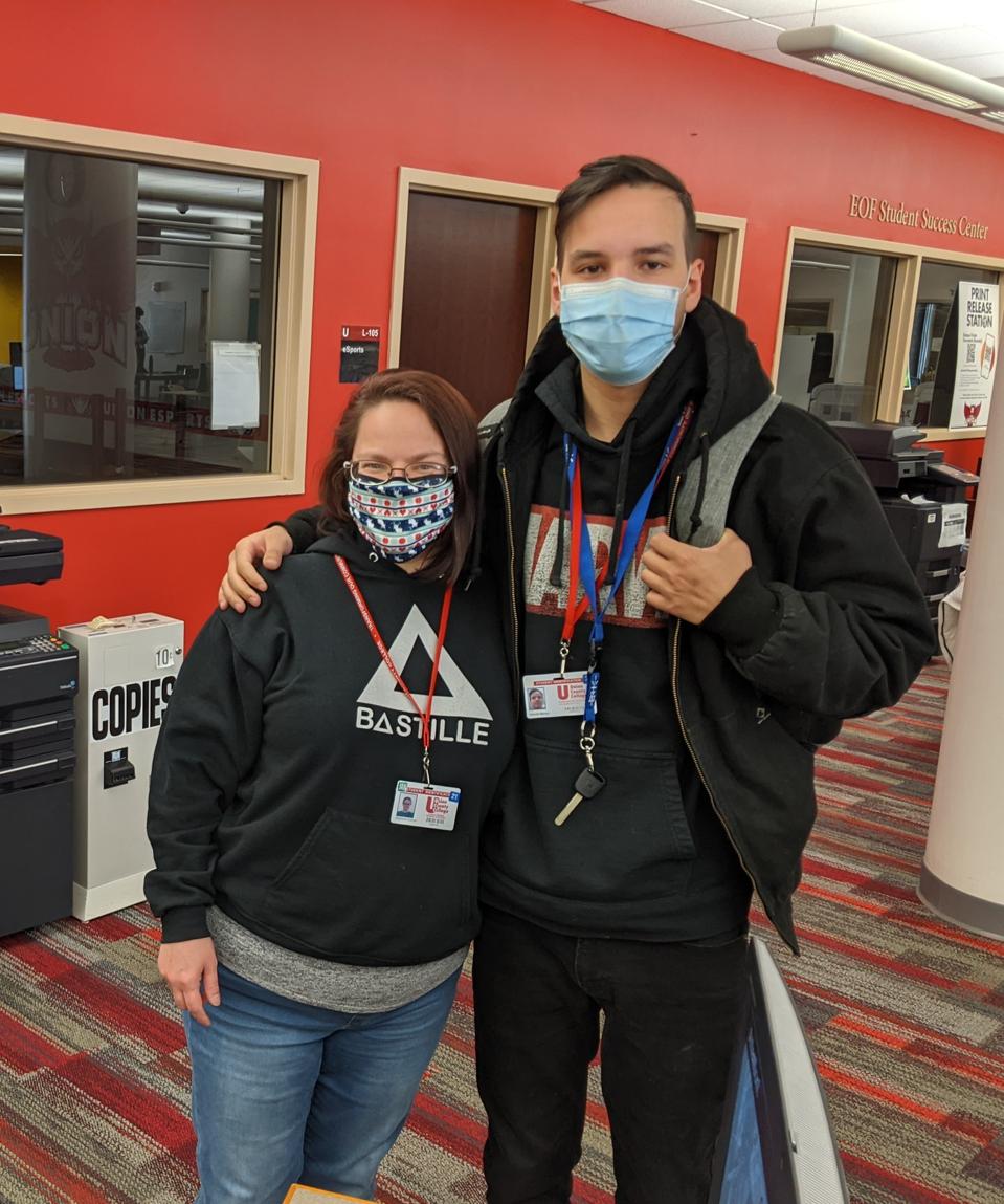 Masked mother and teenage son standing in college library.