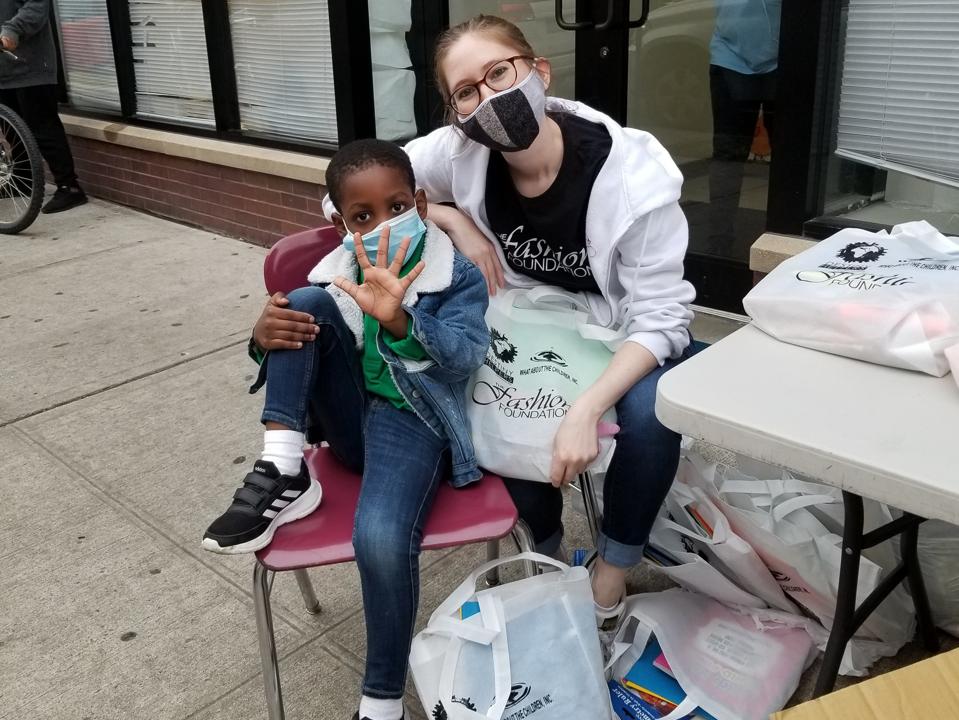 Amanda Munz sits with a young boy, in masks, surrounded by The Fashion Foundation bags.