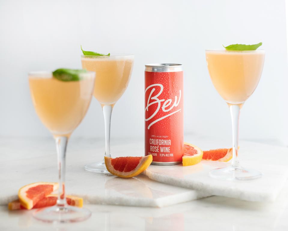 A can of Bev wine sits among three glasses and grapefruit wedges.