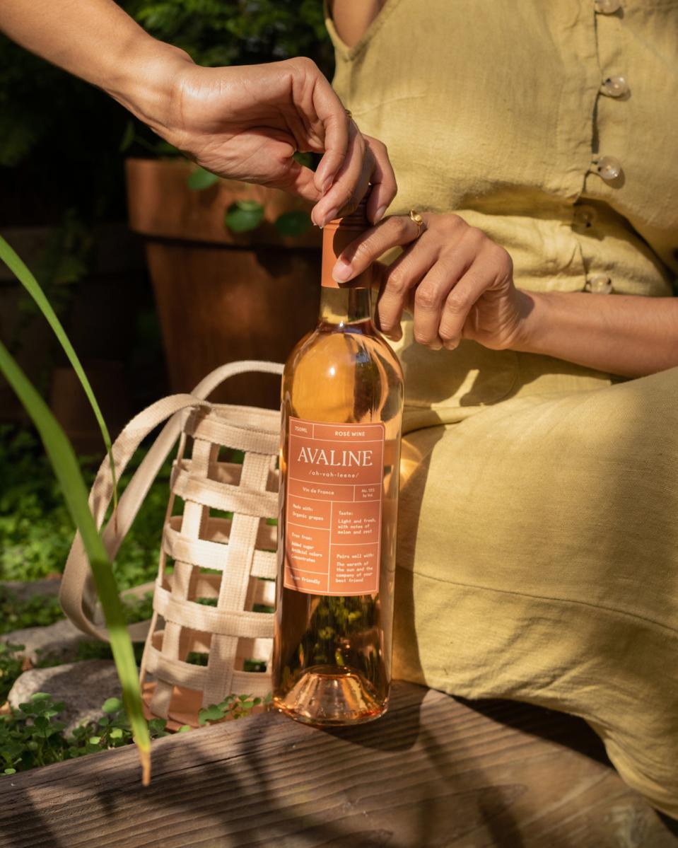 A woman is opening a bottle of Avaline rosé with her purse in the background.