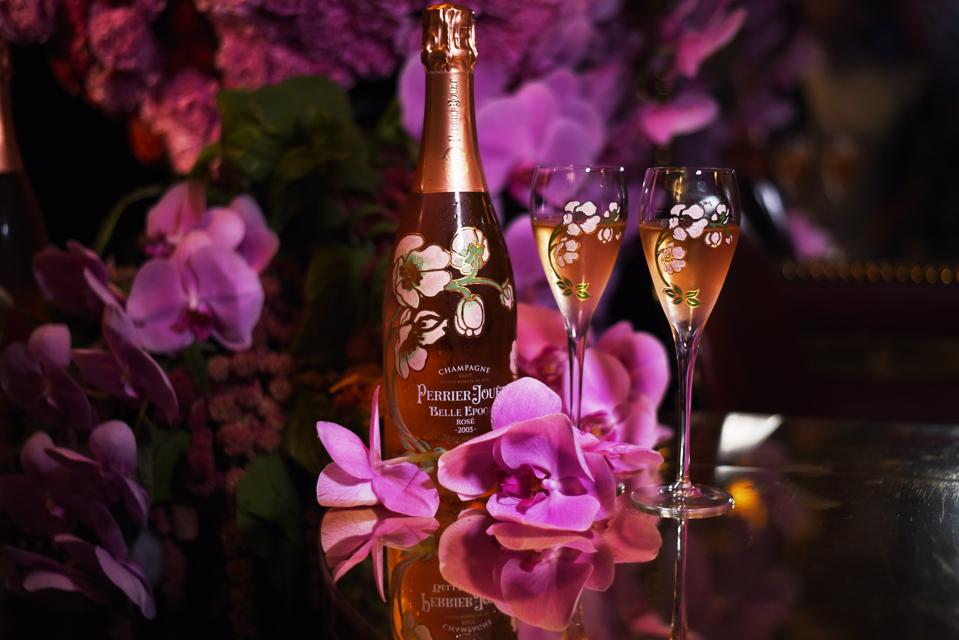 A bottle of Perrier-Jouët Belle Epoque rosé sits on a table with matching floral glasses and flowers.