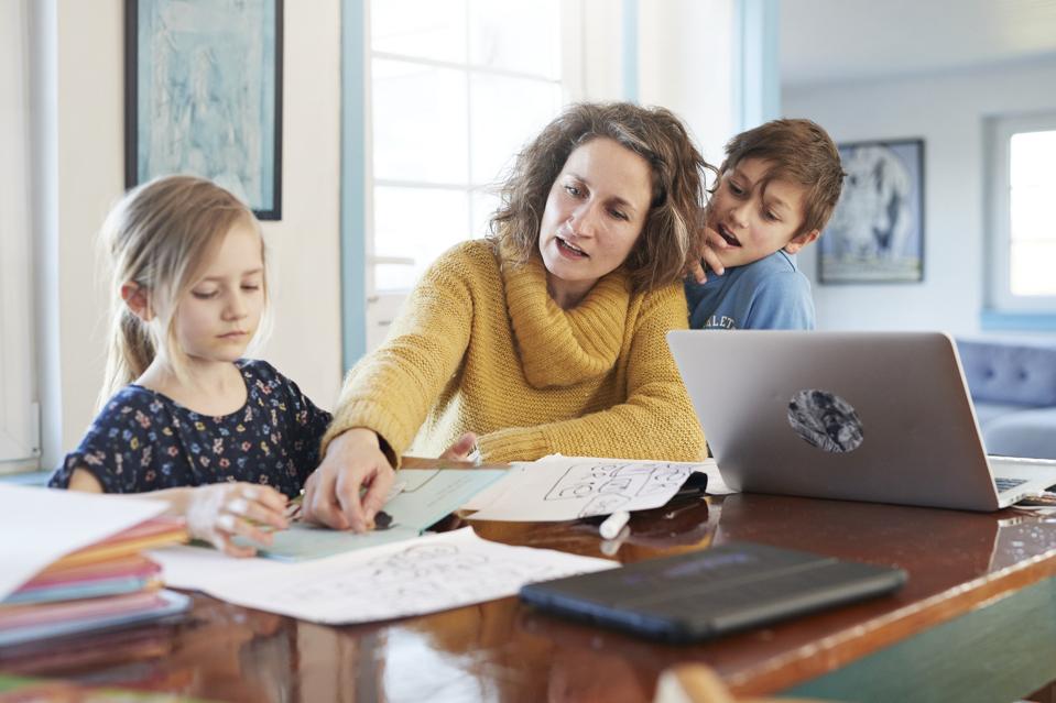 Mother homeschooling daughter and son at dining table