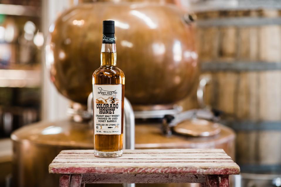 A bottle of whiskey in a distilling room with a copper pot in the background.