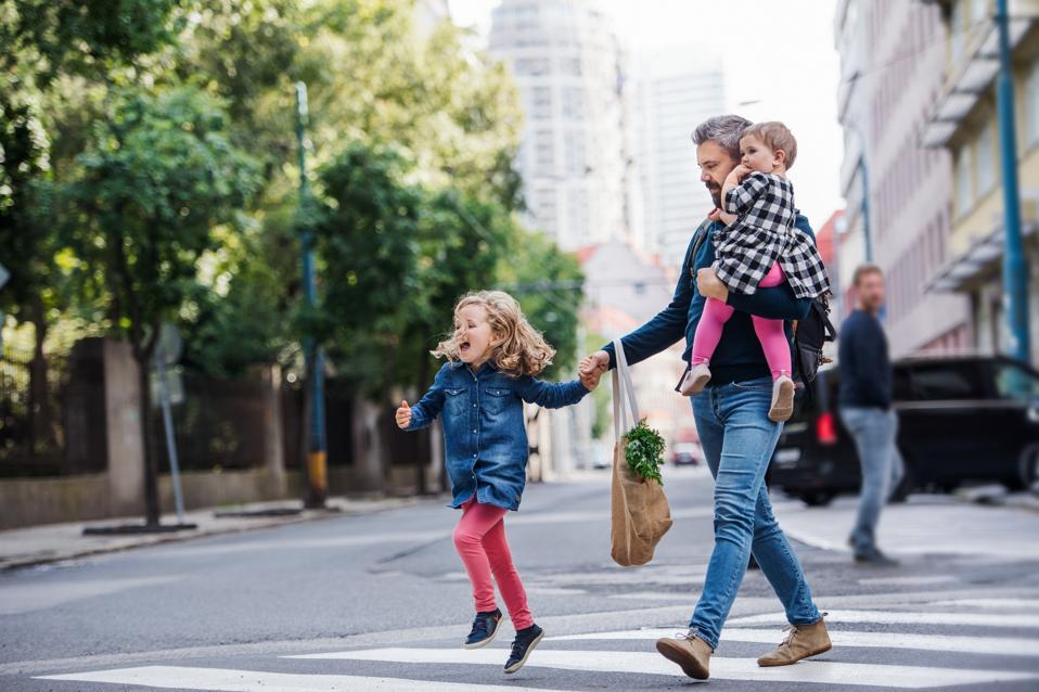 Father with small girls walking outdoors in city, crossing the road.