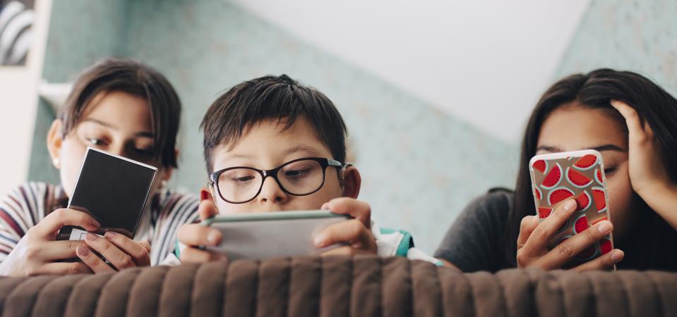 Low angle view of boy looking at digital tablet while lying with sisters using mobile phone on bed at home