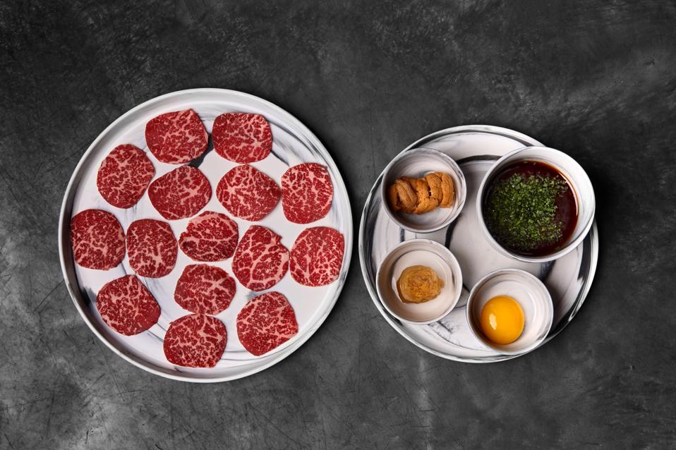 a plate with thinly sliced wagyu, uni, soy sauce, egg yolk fired table side