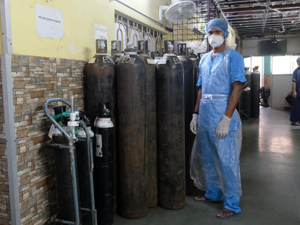 A hospital worker dressed in head to toe PPE stands by a dozen oxygen tanks. 