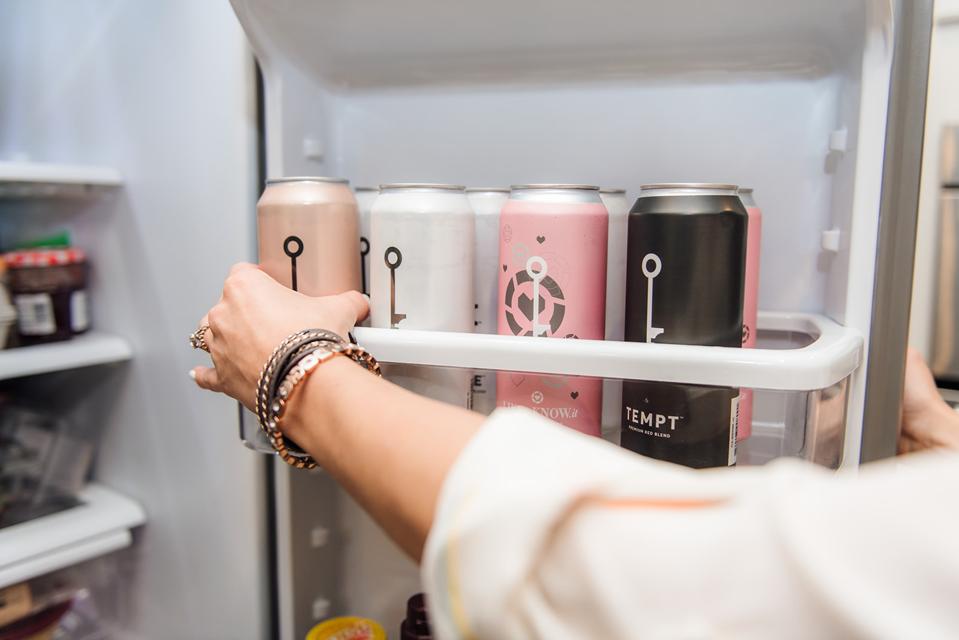 Woman reaching for Wine Society canned wines on refrigerator door