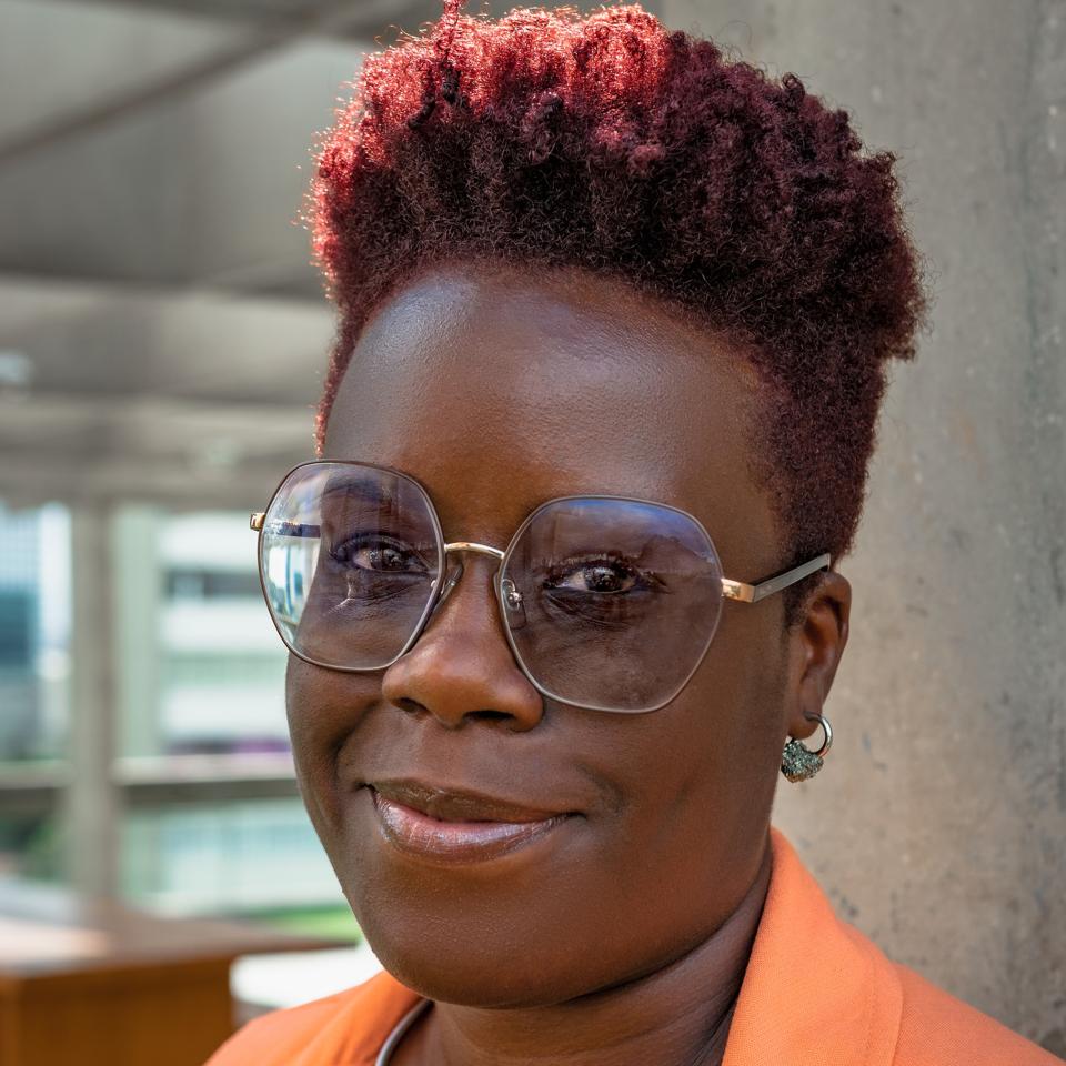 Mita Loreno usa óculos, cabelo curto e uma jaqueta laranja.  Ela é uma mulher negra. 