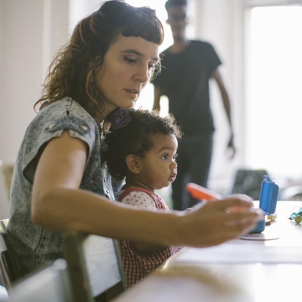 Woman working while sitting with daughter at table in house