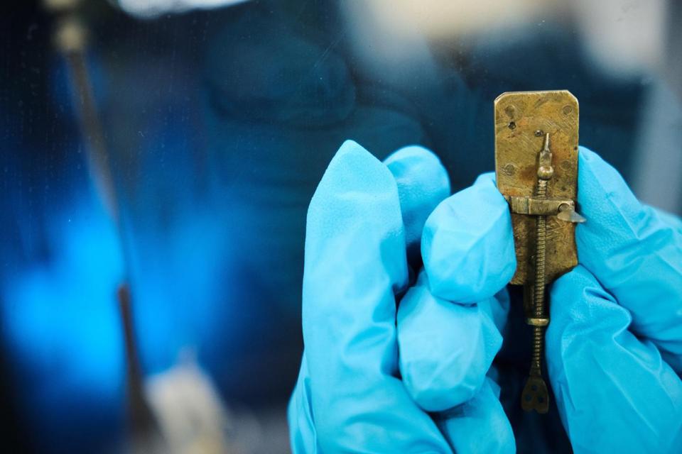 color photo of an early microscope held in a blue gloved hand