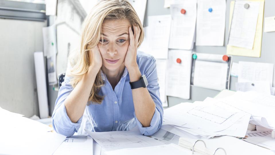 Stressed woman sitting at desk in office surrounded by paperwork