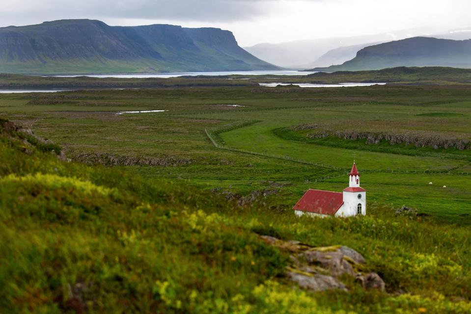 Paisaje islandés con una pequeña iglesia blanca, fiordos y montañas