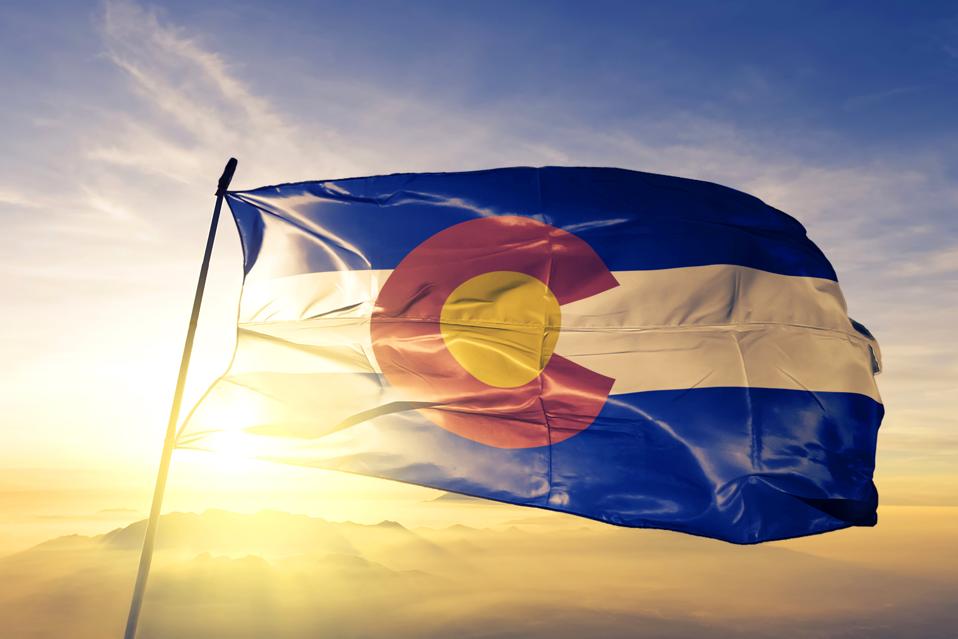 Colorado state of United States flag textile cloth fabric waving on the top sunrise mist fog