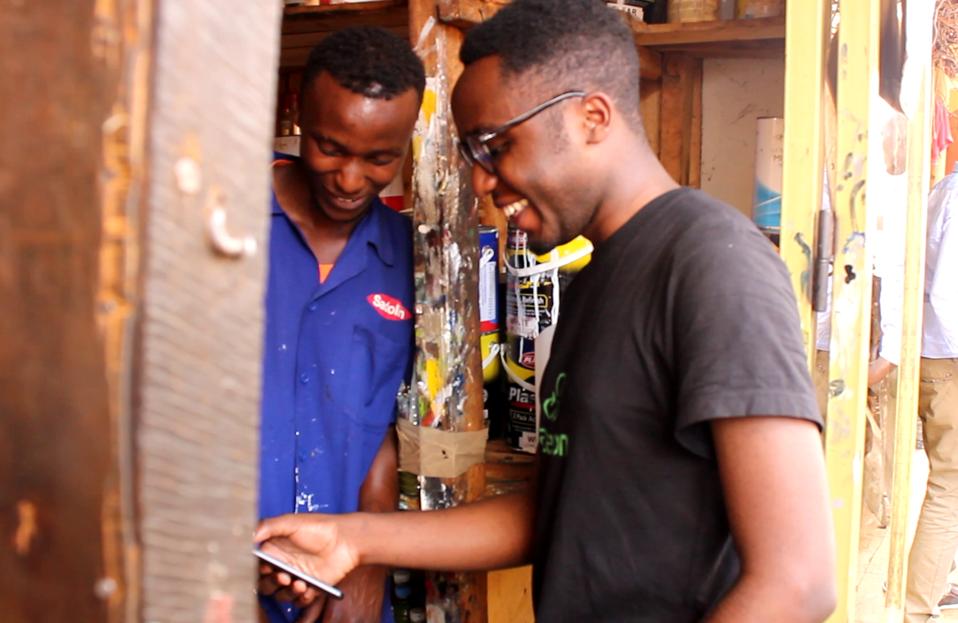 Two Kigali residents smile as one uses an app to confirm delivery of scrap metal.
