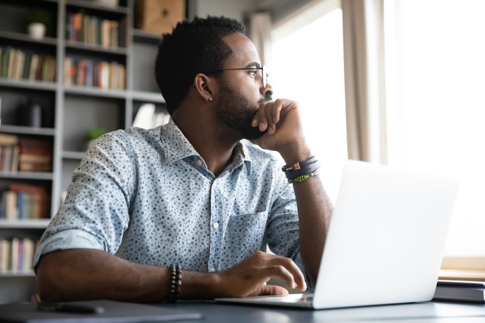 Thoughtful serious man sat with laptop thinking of project