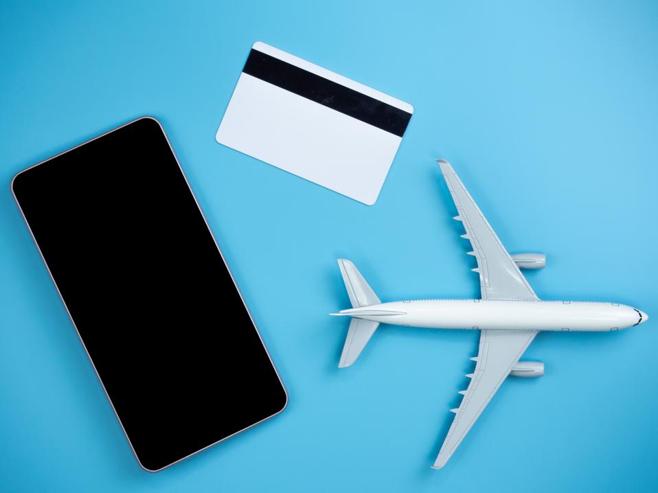 Top view of smartphone, credit card and plane on blue isolated background with copy space.