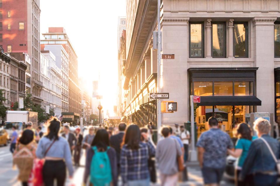 Diverse group of anonymous people walking down busy New York street with bright sunlight shining in the background in New York City