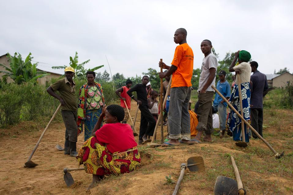 Rwandan villagers carrying tools get together to participate in Umuganda.