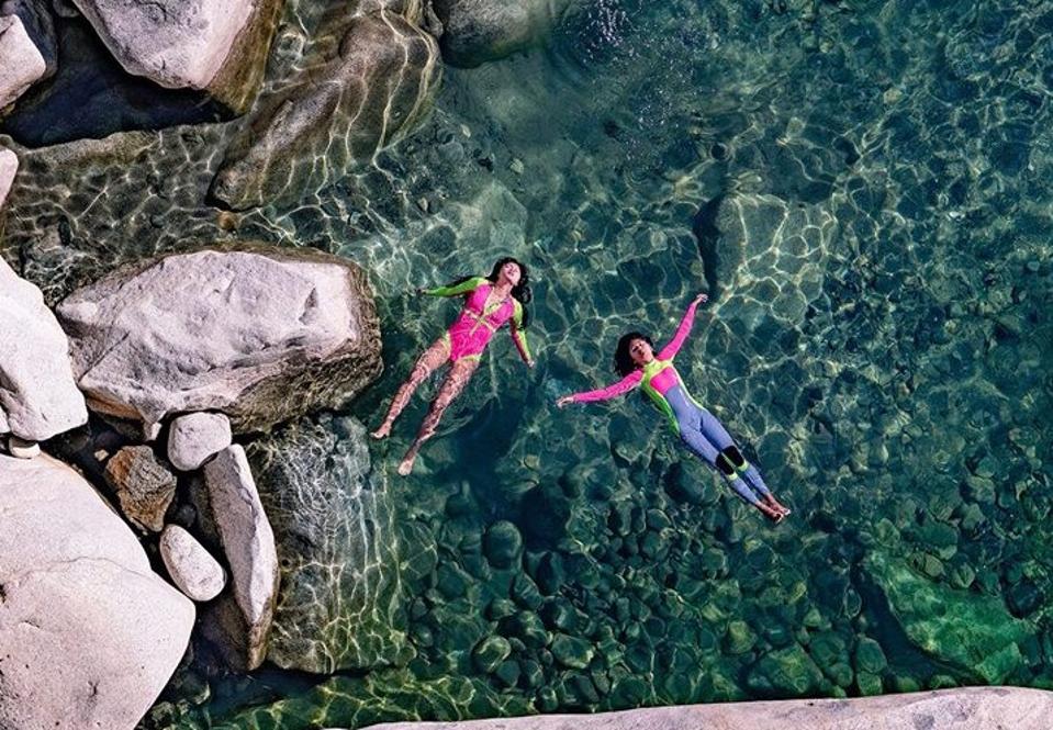 Two people float on their backs in clear water surrounded by boulders