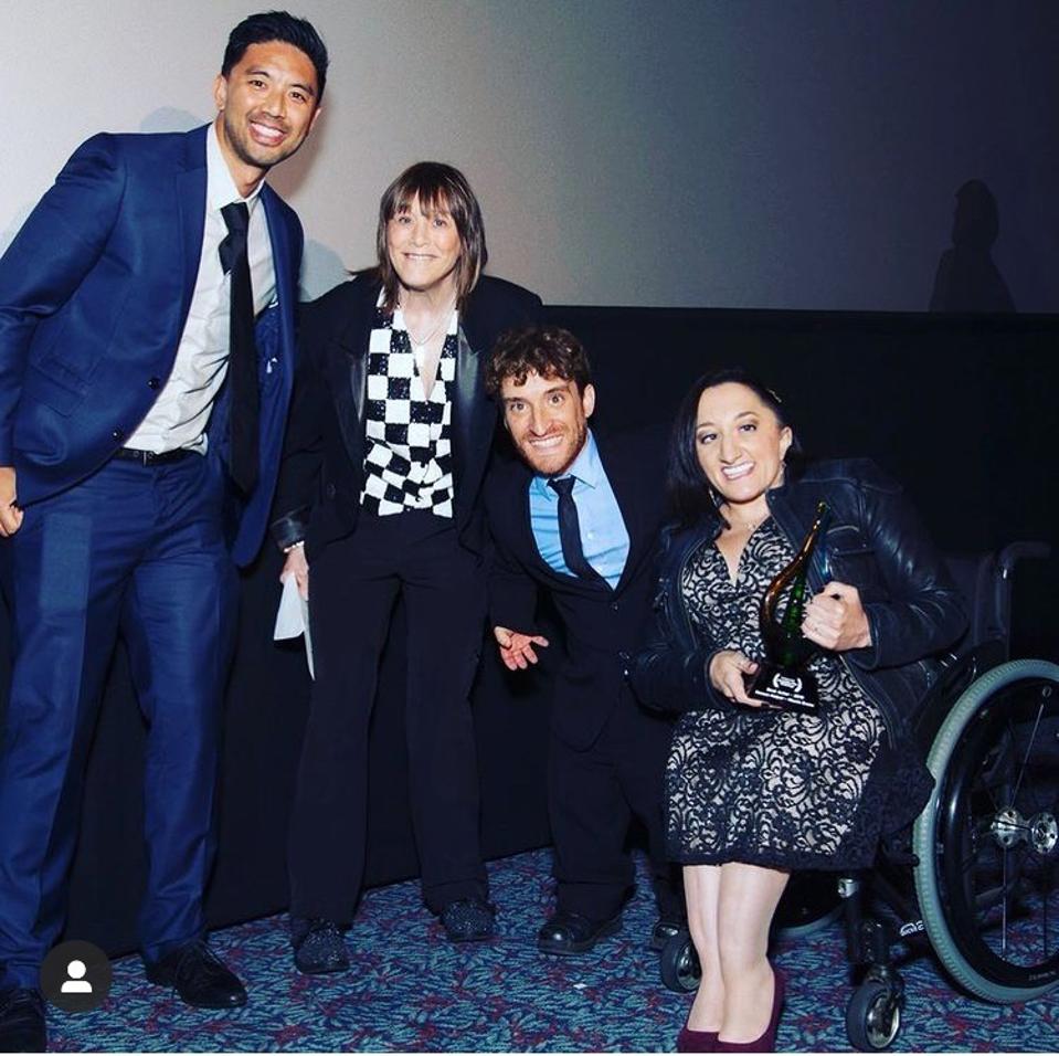 An Asian man, white woman, white man, and white woman in a wheelchair stand together.