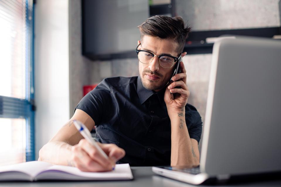 Young man in office working on laptop computer and phone
