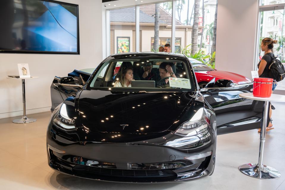 Customers admire a Tesla Model 3 electric vehicle at a Tesla...