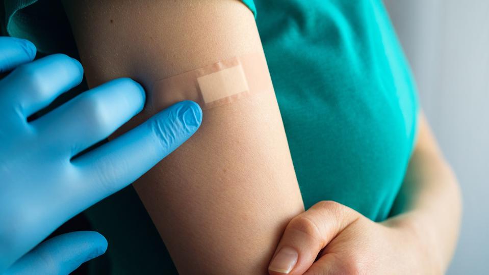 A doctor or health care professional applies a patch or adhesive bandage to a girl or young woman after vaccination or injection of medication. The concept of medicine and health care, vaccination and treatment of diseases. First aid.